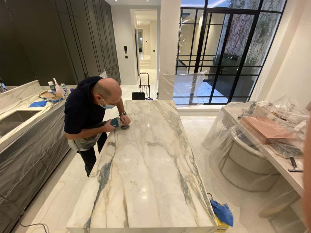 Professional technician polishing marble worktop edge profile using hand-held angle grinder with diamond pad